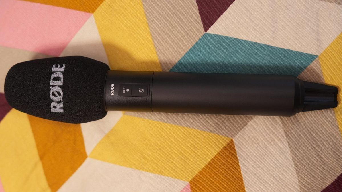 Black RDE microphone with record and mute buttons, resting on a colorful geometric-patterned fabric background.