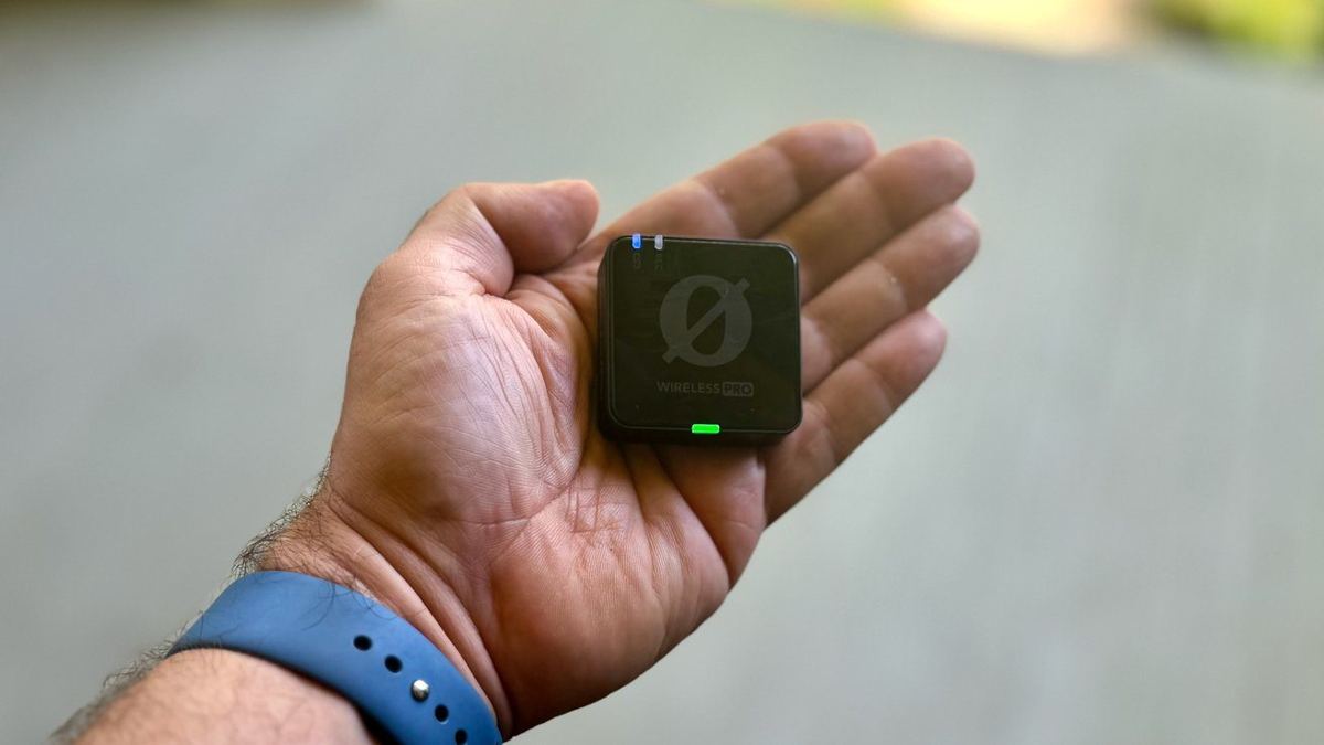 Hand holding a small black electronic device with a green indicator light and the text 'WIRELESS PRO' on it.